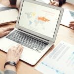 Professional team discussing global marketing strategies with charts and graphs on a laptop.